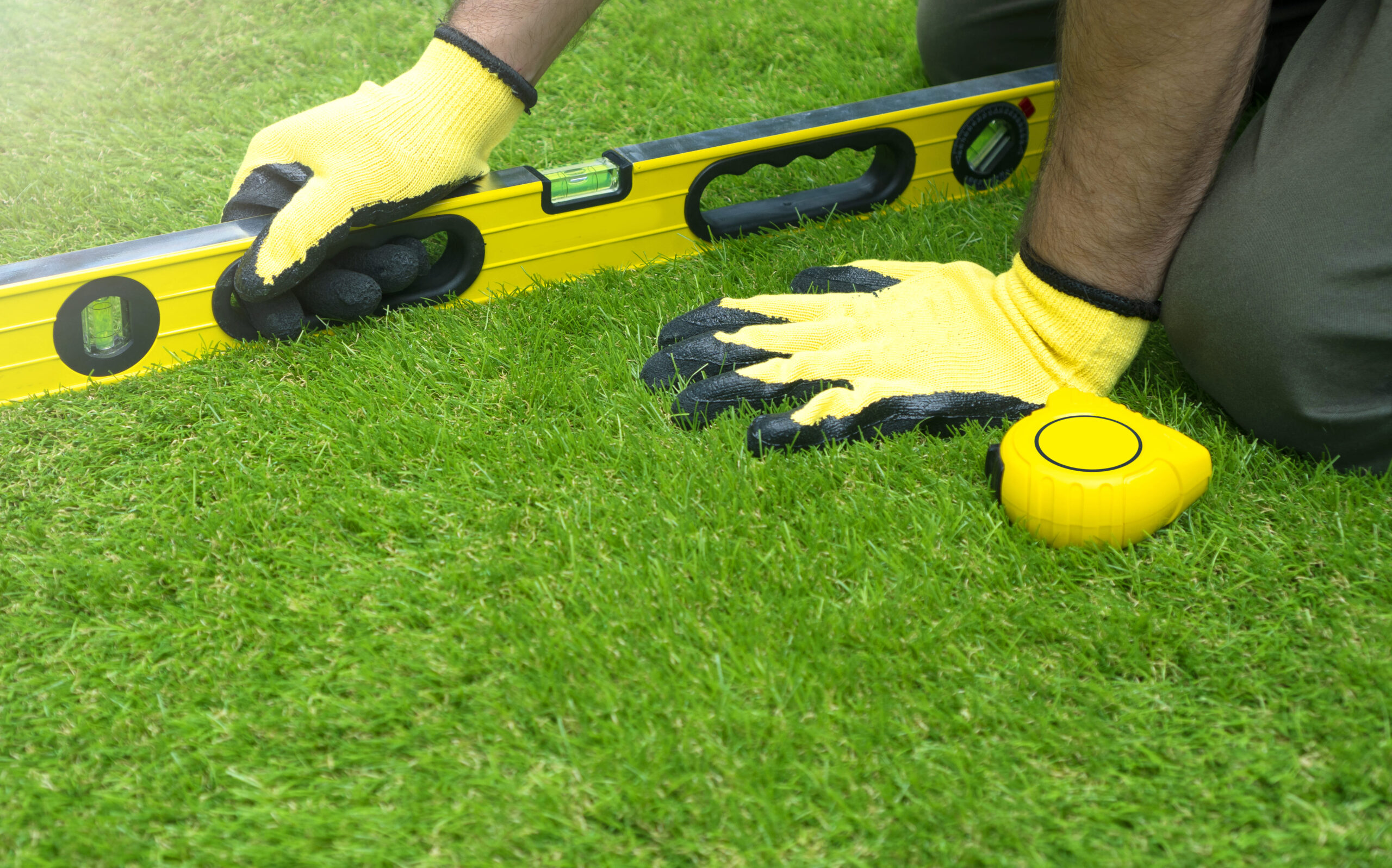A person wearing yellow gloves and holding a level